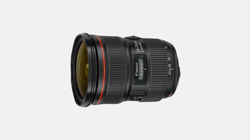 A black Canon EF 24-70mm f/2.8L II USM zoom lens is shown horizontally with its front element slightly angled, against a plain light gray background