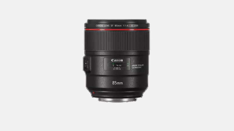 A black Canon EF 85mm f/1.4L IS USM lens with a red ring around its barrel is positioned upright against a plain light gray background