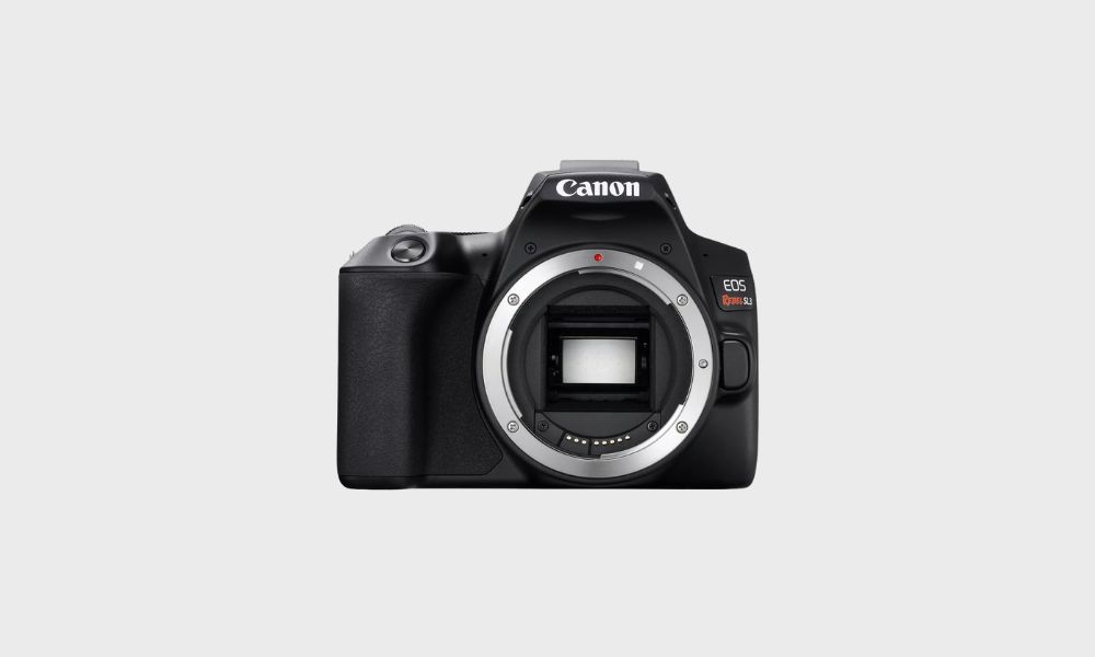 A black Canon EOS Rebel SL3 DSLR camera body, viewed from the front with its lens mount exposed, is set against a plain light gray background