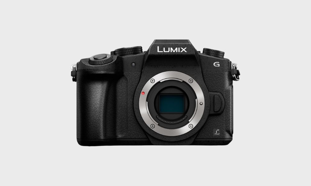 A black Panasonic Lumix G85 mirrorless camera body, viewed from the front with its lens mount visible, is set against a plain light gray background