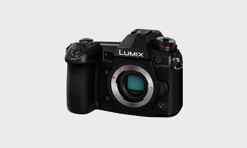 A black Panasonic Lumix G9 mirrorless camera body, viewed from the front at a slight angle, with its lens mount visible, is set against a plain light gray background