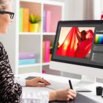 Woman editing a vibrant fashion photo on a desktop computer in a modern, brightly lit workspace.