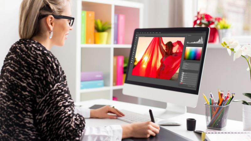 Woman editing a vibrant fashion photo on a desktop computer in a modern, brightly lit workspace.