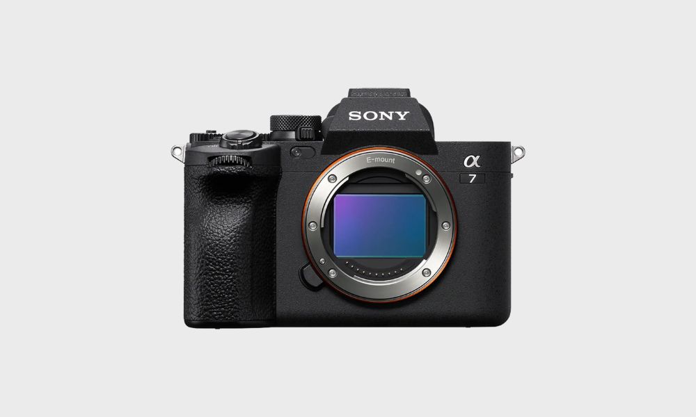 A black Sony Alpha a7 IV mirrorless camera body, viewed from the front with its E-mount lens opening and sensor visible, is set against a plain light gray background