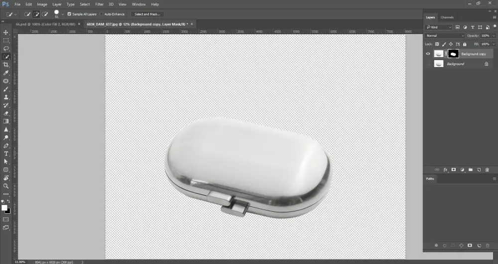 A Photoshop screenshot shows a metallic, oval-shaped object, possibly a pill case, isolated on a transparent background, indicated by the grey and white checkerboard pattern. The layers panel on the right shows "Background copy" with an attached layer mask, and "Background" underneath. The layer mask thumbnail is visible next to the "Background copy" layer