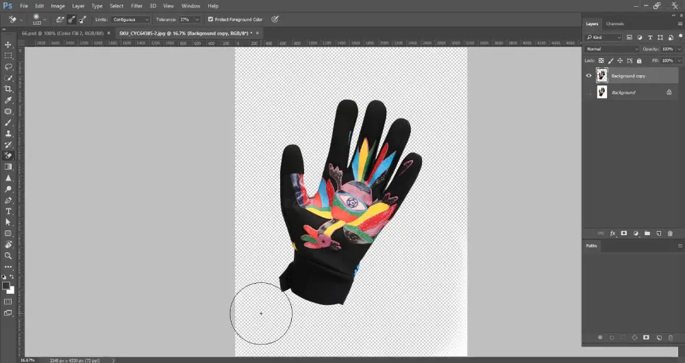 A Photoshop screenshot displays a black cycling glove with a vibrant, colorful design on the palm, now largely isolated on a transparent background, indicated by a checkerboard pattern. A circular brush cursor, from the Background Eraser Tool, is positioned near the bottom left of the glove, suggesting continued background removal. The layers panel on the right shows "Background copy" and "Background" layers