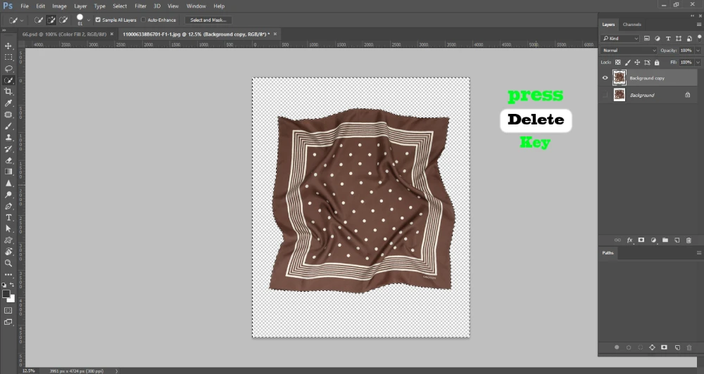 Screenshot of Adobe Photoshop showing a brown polka-dotted scarf with the background removed, leaving a transparent checkerboard area. The selection marquee still surrounds the scarf. On the right, the "Layers" panel displays two layers: "Background copy" and a locked "Background." Bright green and white text on the image instructs to "press Delete Key."
