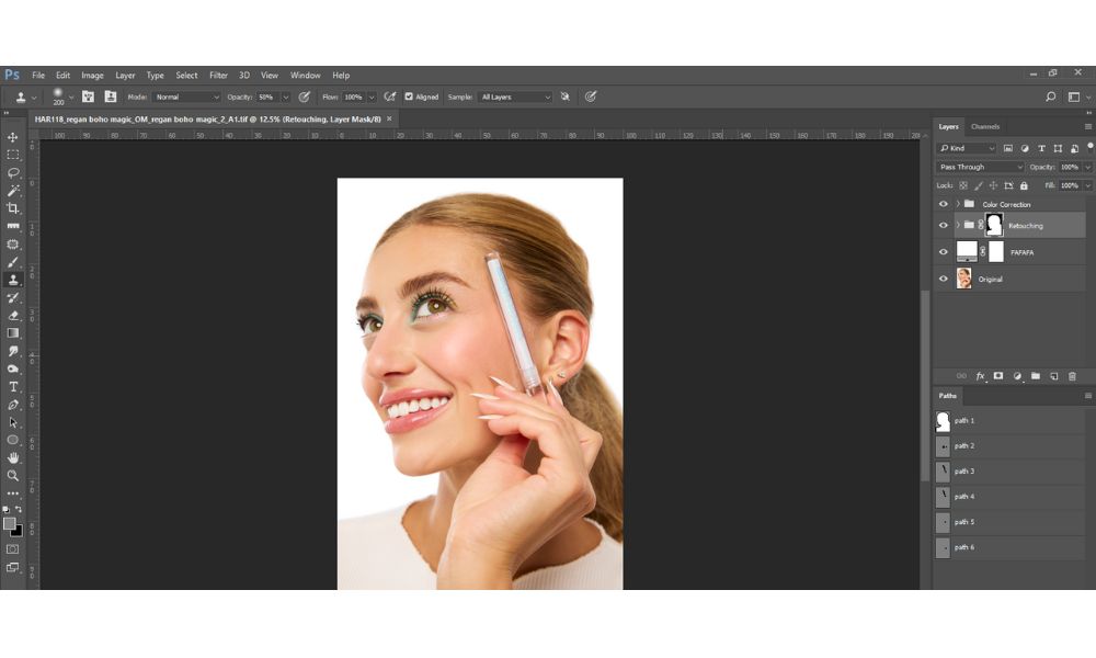 A screenshot of Photoshop showing a close-up portrait of a smiling woman being edited. Her face is bright and clean, and she is holding a makeup brush near her cheek. The Photoshop interface with layers and tools is visible around the image