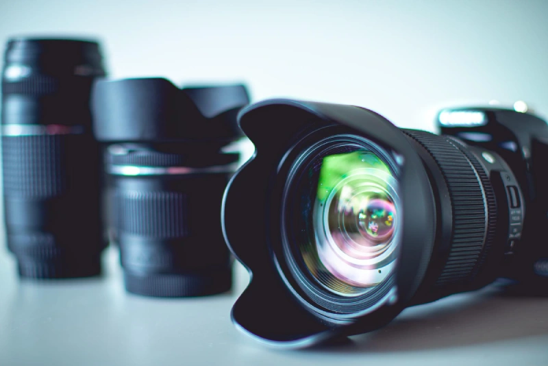 Close-up of a DSLR camera with a wide-angle lens and lens hood, placed on a table alongside three other interchangeable camera lenses in the background