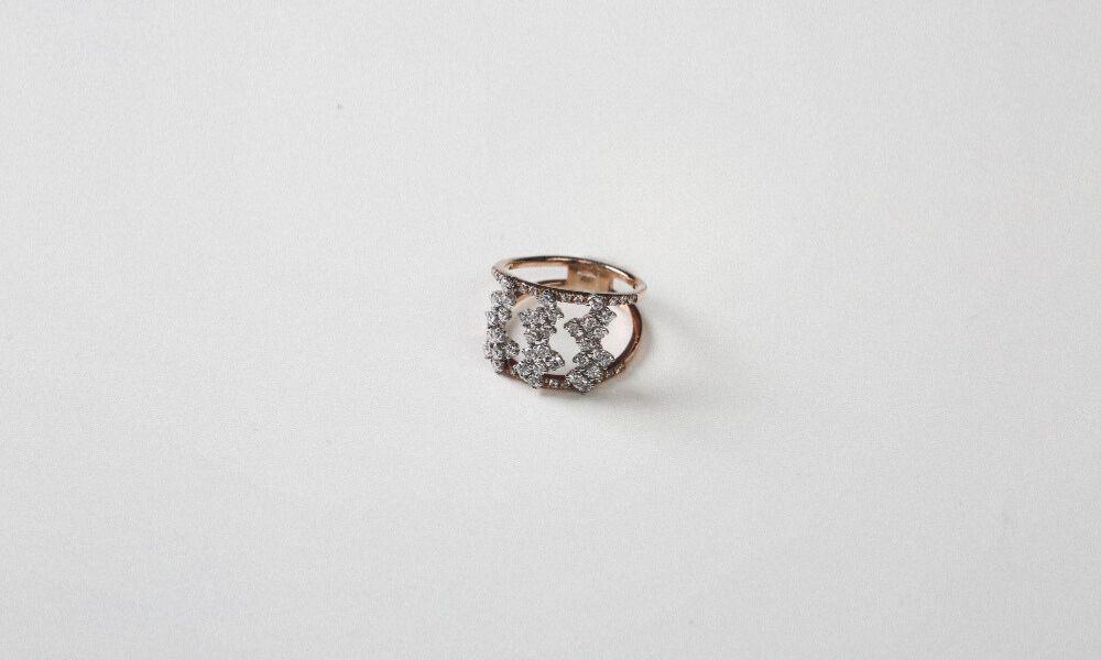 A top-down shot of a rose gold ring adorned with clusters of small, sparkling diamonds, set against a plain white background