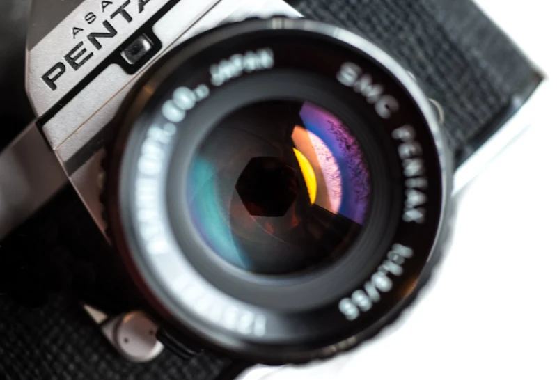Close-up view of a vintage Pentax camera lens showing a wide aperture opening with colorful light reflections on the glass elements