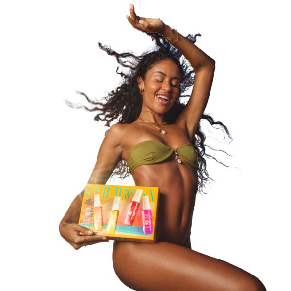 Joyful woman with curly hair in a green bikini, holding an orange box of colorful spray bottles against a white background.