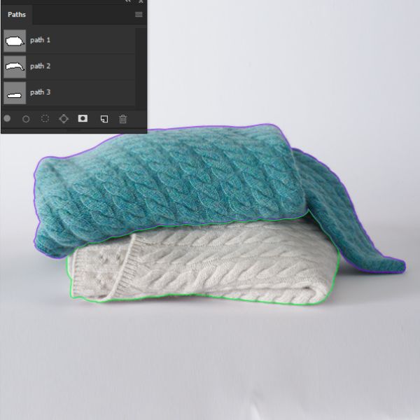 Two cable-knit sweaters, one turquoise and one light grey, are stacked on a white surface. Overlaid on the image are colored outlines (purple and green) tracing the shape of the sweaters, indicating active clipping paths from an editing software panel shown in the top left corner