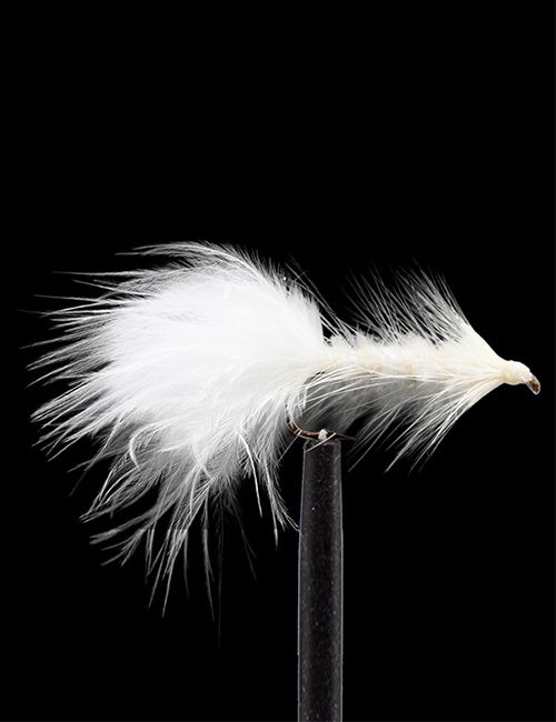 A detailed close-up of a white feathered fly fishing lure with a barbed hook, held upright by a black tool against a stark black background.