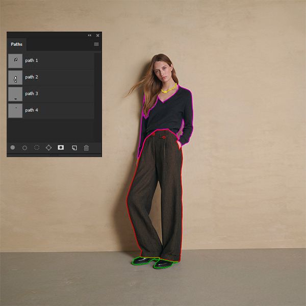 A woman wearing a dark V-neck top, dark brown wide-leg trousers, and black shoes stands against a beige wall. Overlaid on the image is a "Paths" panel from an editing software, with colored outlines (pink, red, green, yellow) around her clothing and shoes, indicating multiple clipping paths