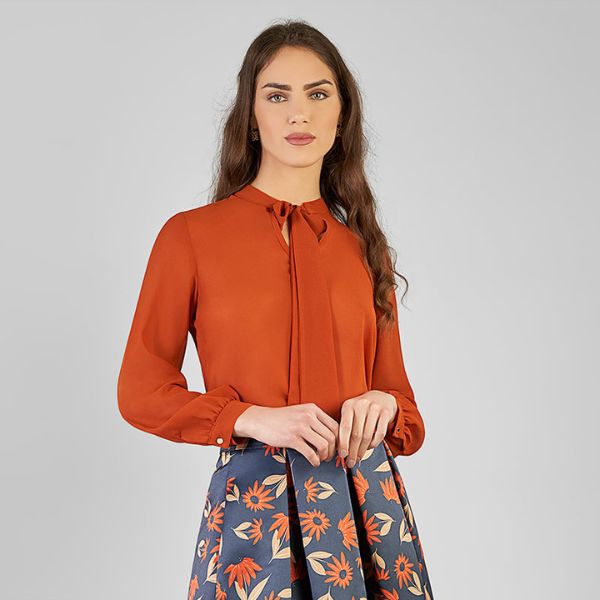 Retouched portrait of a female model wearing a rust-colored blouse and floral skirt against a plain background.