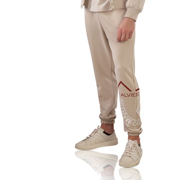 Legs in beige sweatpants and light sneakers stand on a pure white background with a reflective shadow