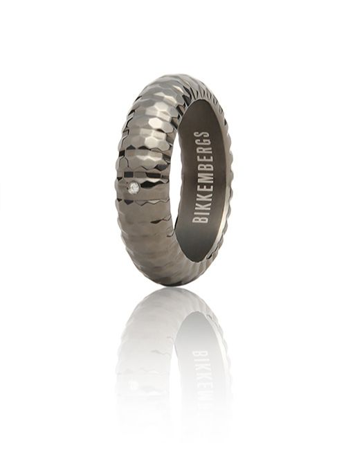 A dark, textured ring with a small diamond and "BIKKEMBERGS" engraved on the inside, cast with a soft reflection on a white surface.