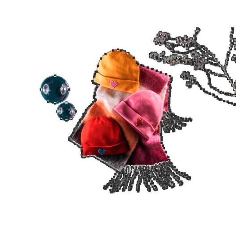 A flat lay of three knitted beanies—red, orange, and pink, each with a small blue heart patch—arranged on a striped scarf with white fringe. The items have green and purple outlines, indicating active clipping paths from editing software, and some transparent bubbles and a branch of berries with pixelated outlines are also visible against a white background