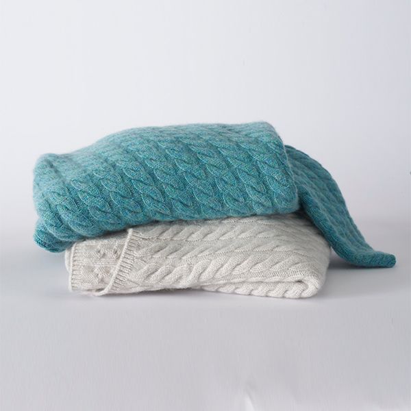 Two cable-knit sweaters, one turquoise and one light grey, are neatly folded and stacked on a white surface