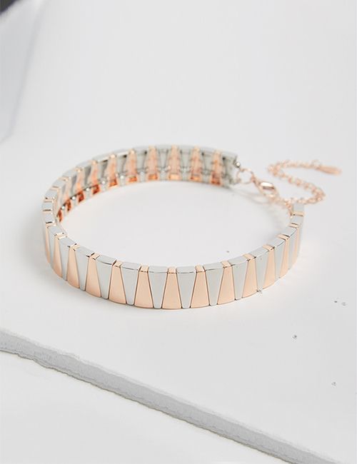 A modern bracelet with alternating rose gold and silver-colored rectangular segments, lying on a light, textured surface