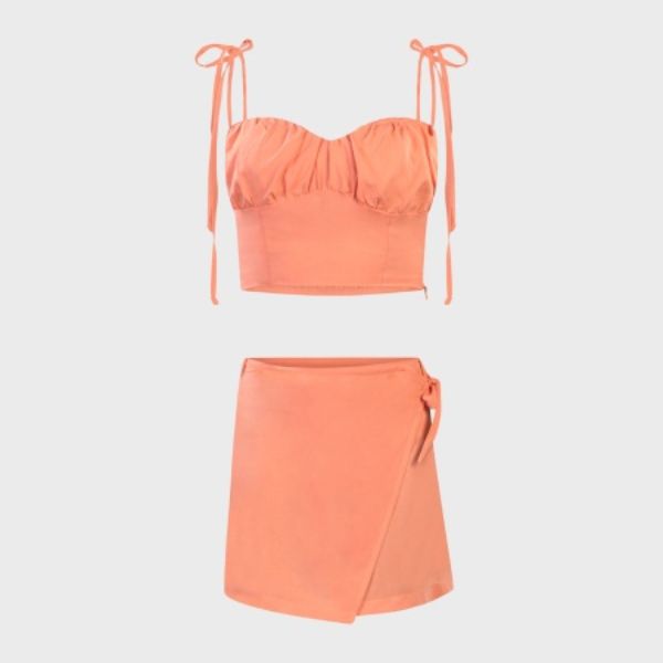 An orange two-piece outfit, consisting of a cropped camisole with shoulder ties and a wrap-style mini skirt, displayed as if on an invisible mannequin against a grey background